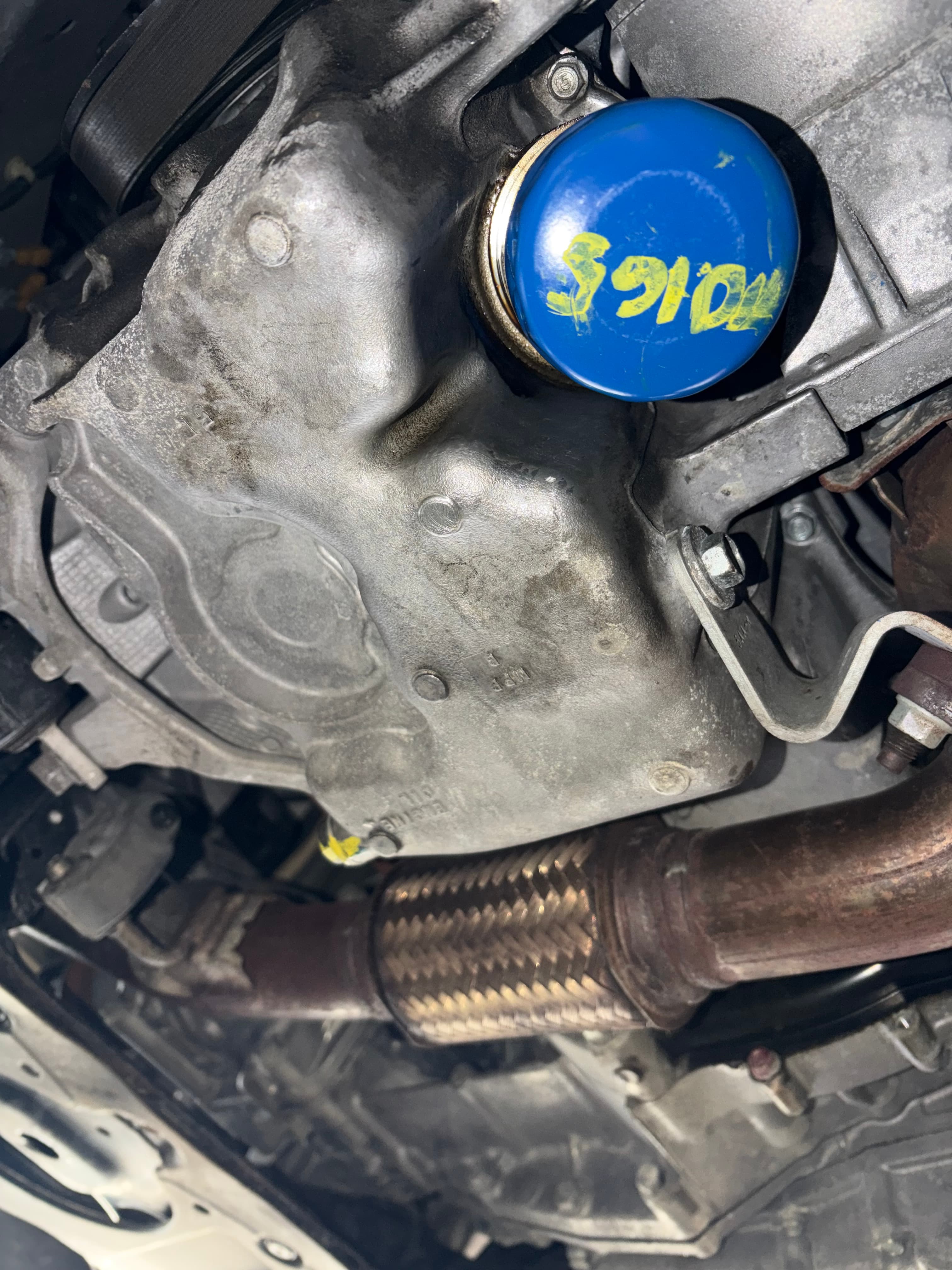 Blue oil filter with yellow writing installed on a silver engine block next to exhaust.