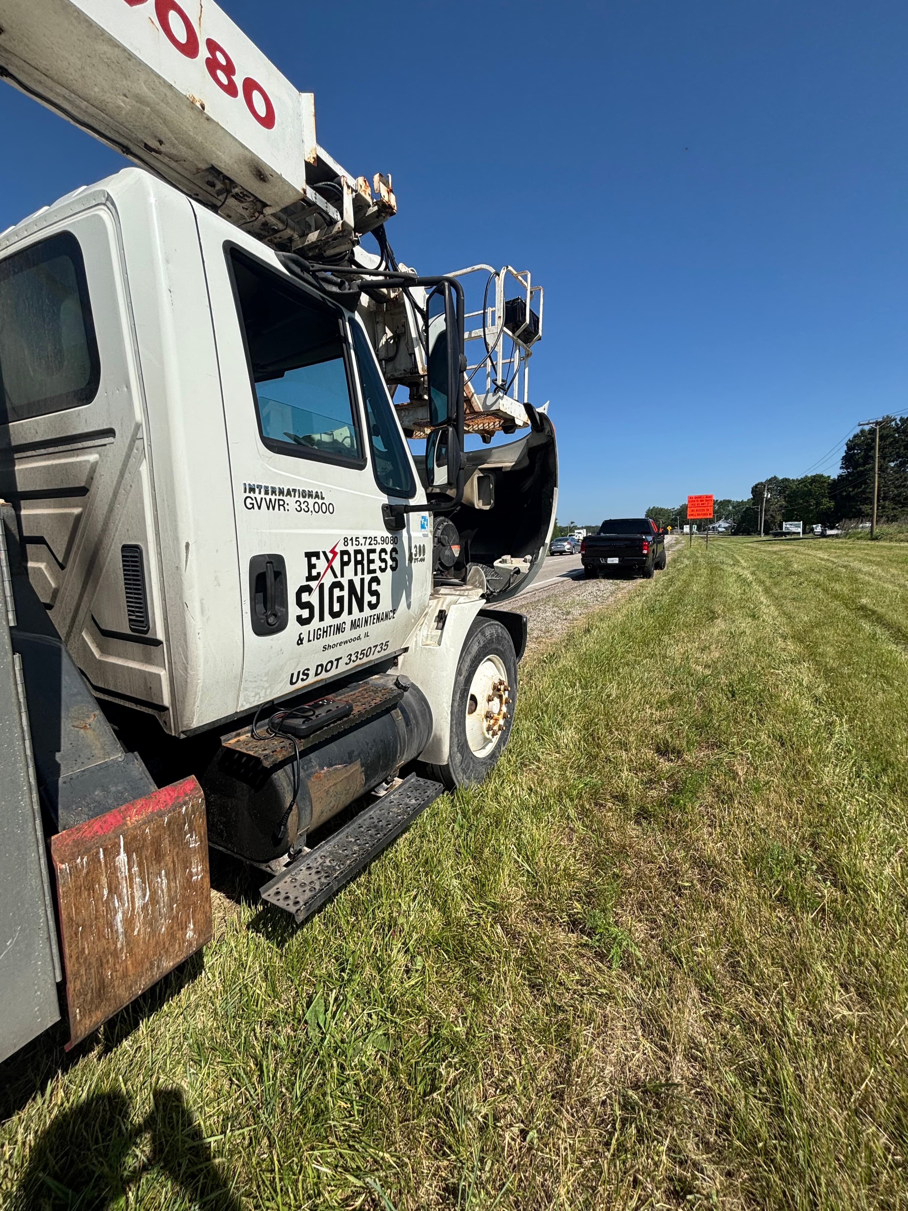 White Express Signs utility truck with open hood parked on a grassy roadside.