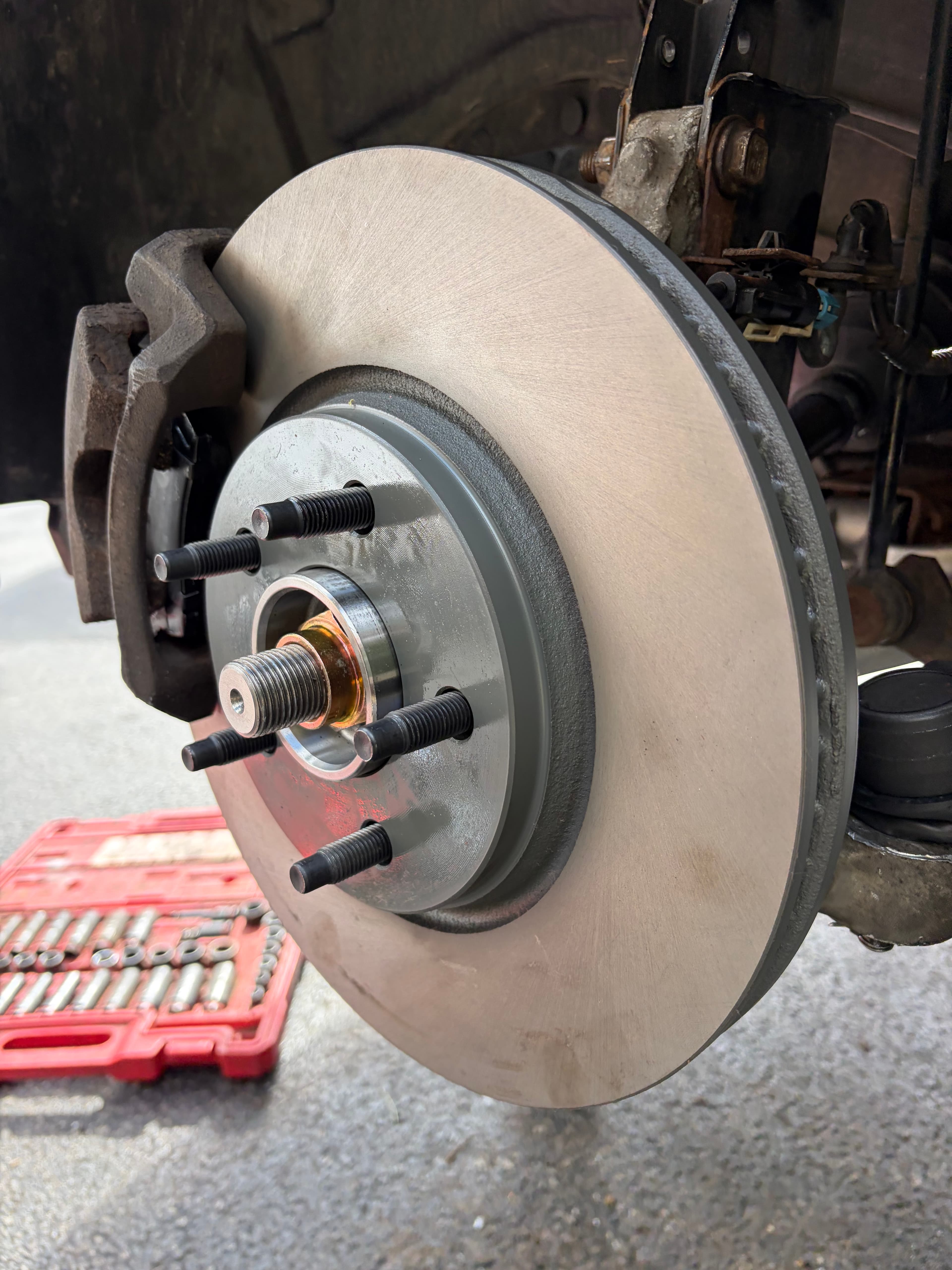 Newly installed silver brake rotor and wheel hub assembly with five black lug studs.