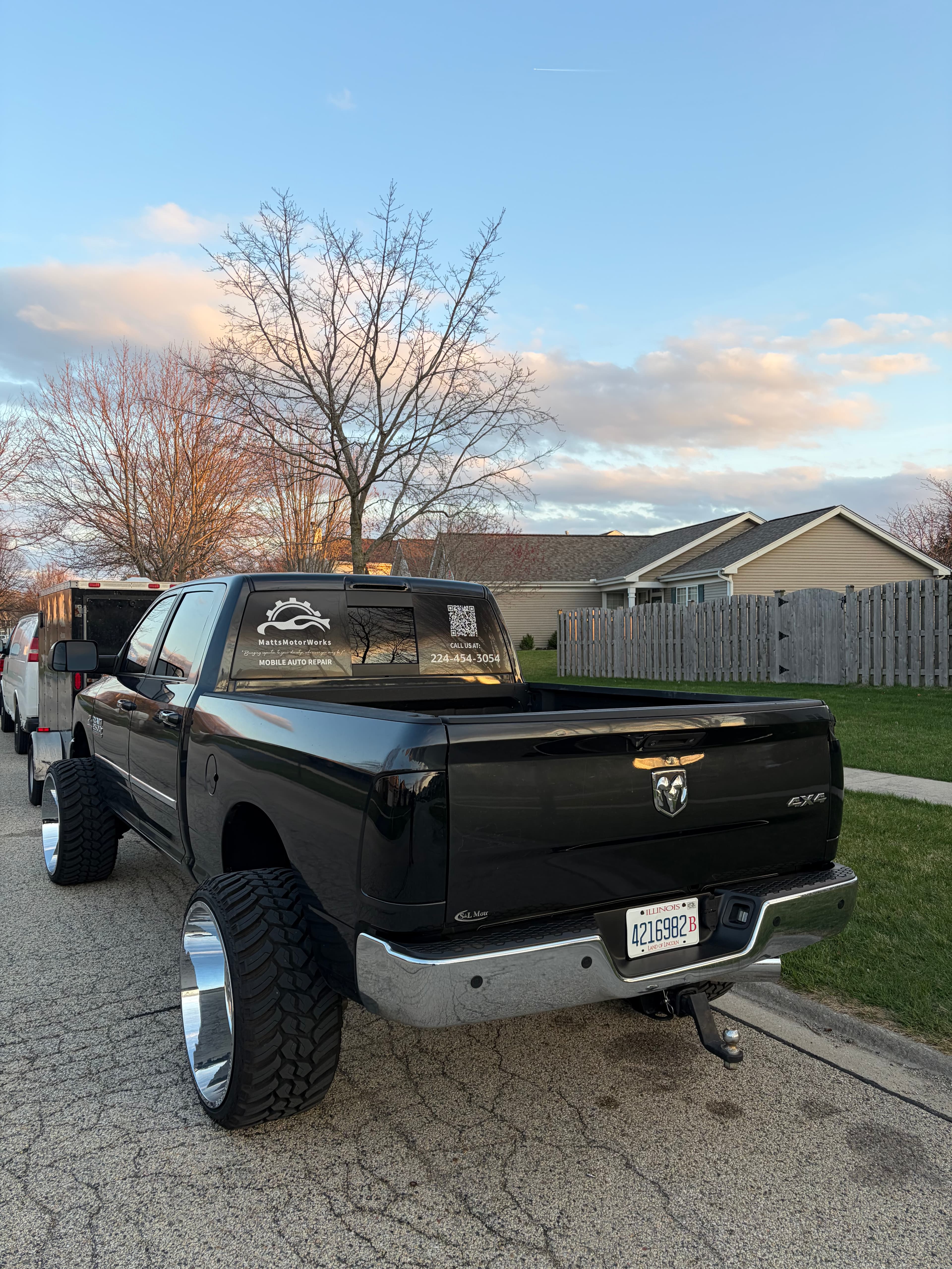 Black Ram pickup truck with large tires and mobile auto repair decals parked at sunset.