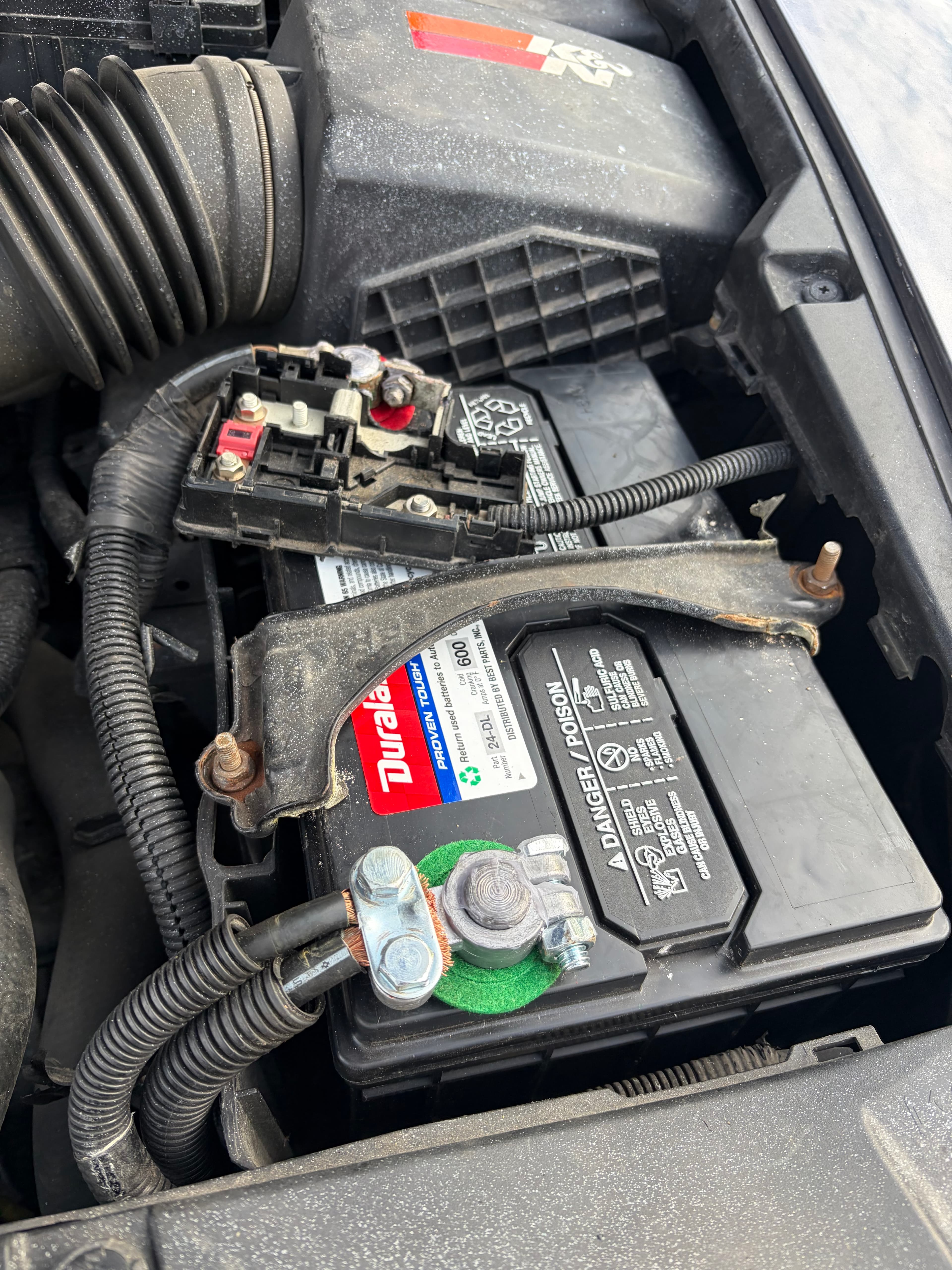 Duralast car battery in an engine bay with connected terminals and a green washer.
