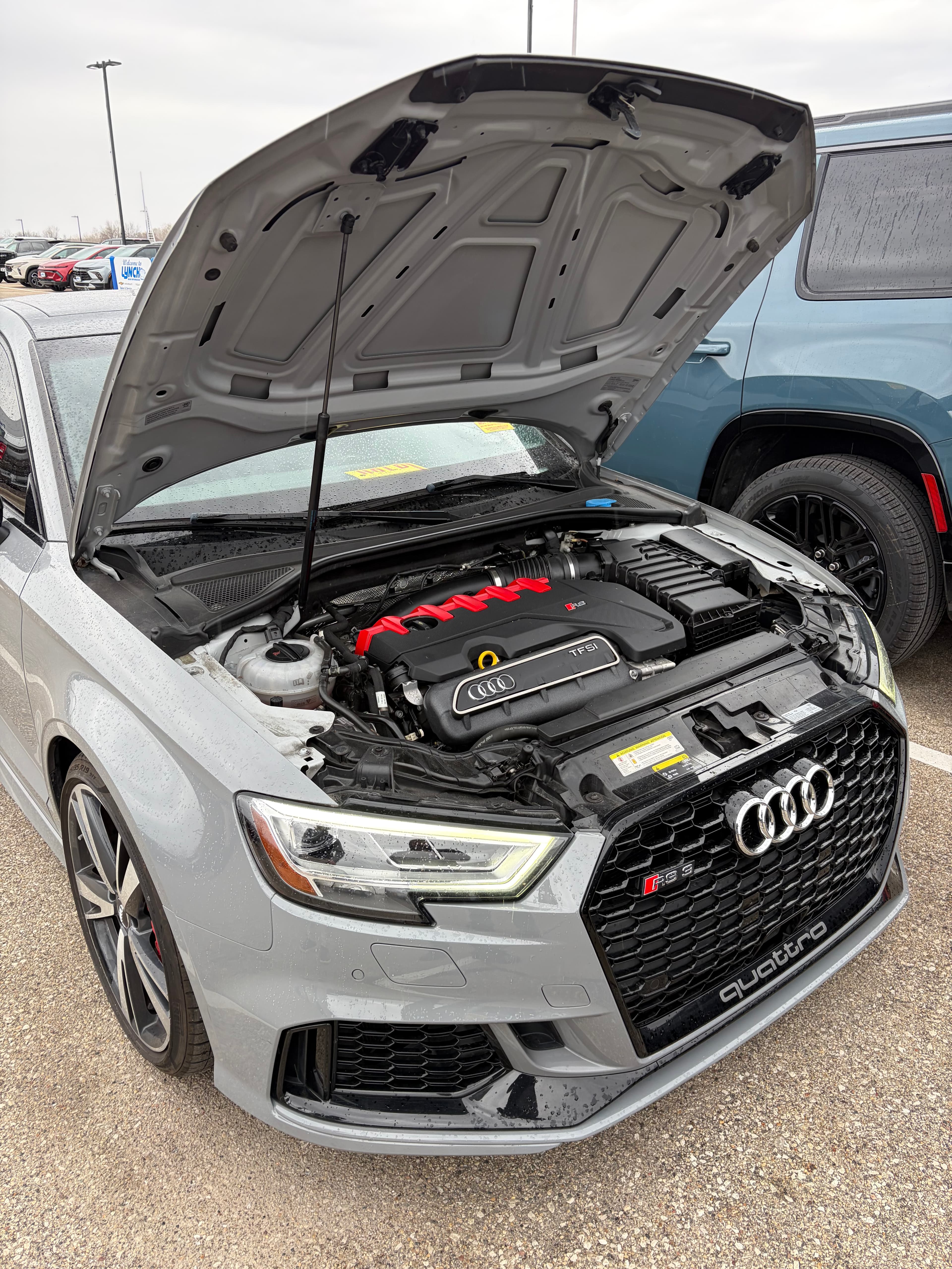 Grey Audi RS3 with an open hood, showcasing the engine and red ignition coils.